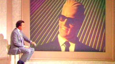 Terry Wogan sits next to a screen showing Max Headroom.