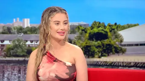 Chloe Ayling smiles, sitting connected  the reddish  Breakfast sofa