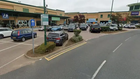 Google Westgate Shopping Park, featuring a number of large stores with a car park in front next to an access road.