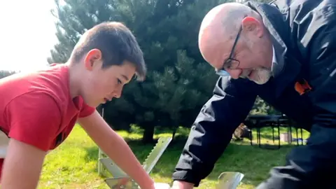 A boy and a man lean over while sawing a log