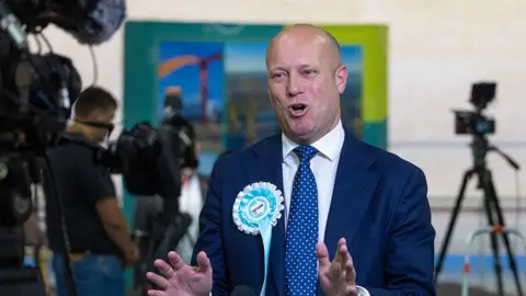 Getty Images Dan Thomas MS, Reform Wales leader, wearing a suit and Reform UK rosette, speaking to journalists