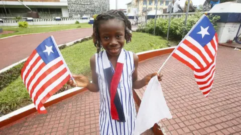 EPA A girl poses with Liberian national flag on the National flag day in Monrovia, Liberia, 24 August 2021