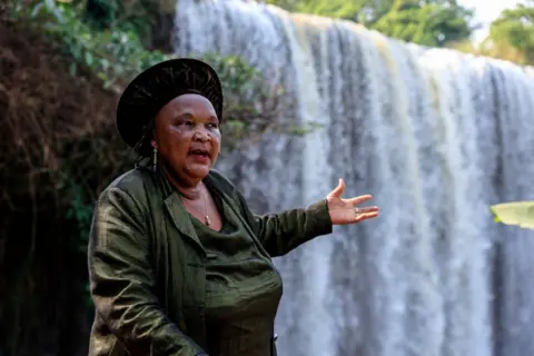 DANIEL BELOUMOU OLOMO / AFP A woman gestures towards a powerful waterfall.