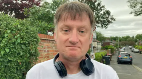 Man with brown/grey hair and a white t shirt.