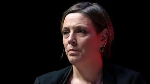 Jess Phillips MP. pictured against black background, looks off to the side 