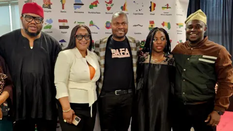 BAFA Media A group of six people, all from an African-Caribbean background, stand smiling in front of a display board which has the names and flag style maps of various African countries on it.
