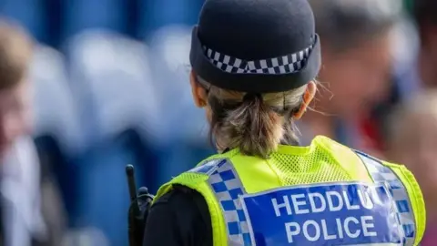 Getty Images A female police officer wearing a hat and uniform faces away from the camera. Her uniform reads: HEDDLU POLICE