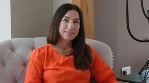 Shaun Whitmore/BBC Dr Beth Mosley sits in a chair and looks towards the camera. She has long dark hair and wears an orange top.