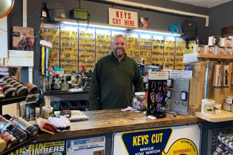 BBC / Naj Modak Scott Robinson stood behind the counter of his business, Robinson's Shoe Repairs