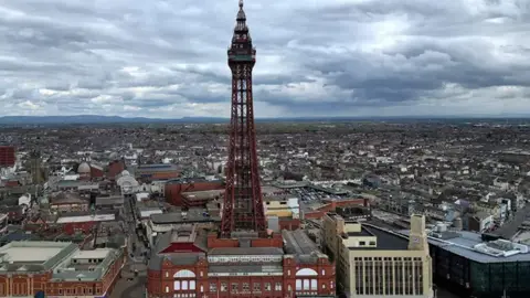 Reuters Aerial shot of Blackpool Tower taken from the front of the Blackpool Tower buildings from the beach. It is a cloudy day and shows the rest of the town in the distance.