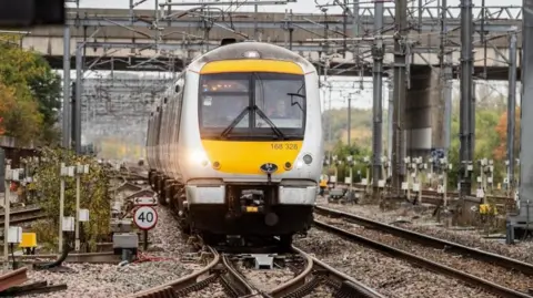 A yellow and silver train running on a track between Oxford and Milton Keynes, part of the planned wider East West Rail project