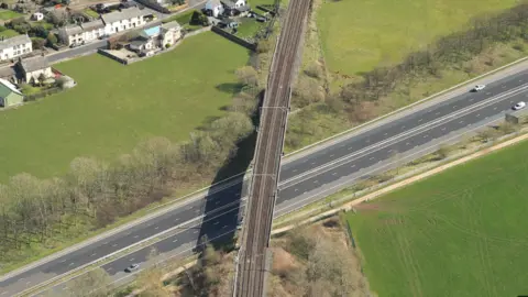 An aerial view of Clifton bridge going over the M6. It is a long, two-track railway bridge, with residential houses to the left. 