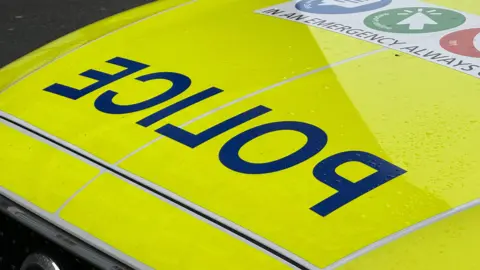 The bonnet of a police car, with the word police in reverse lettering on a yellow fluorescent panel.