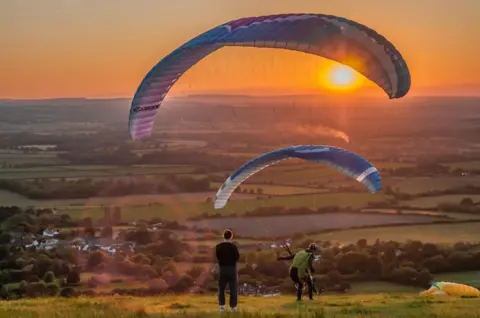David Burr/Alamy People paragliding at sunset at Devil's Dyke on the South Downs, Sussex, England, UK. 8th June 2024.