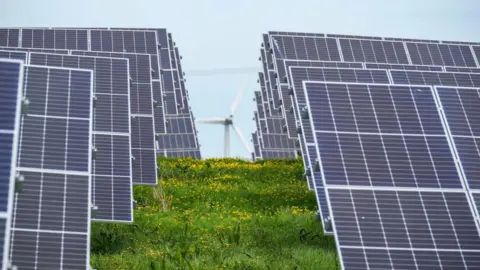 Solar panels in rows in a field with a wind turbine in the distance