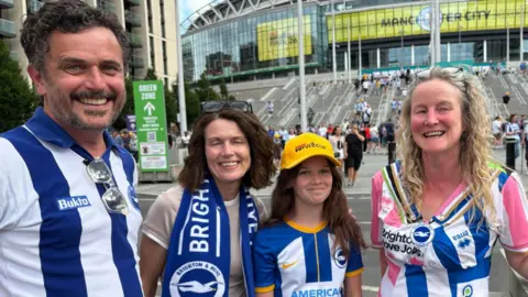 A family wearing Albion shirts and scarves standing for a photo at the base of the steps outside Wembley stadium