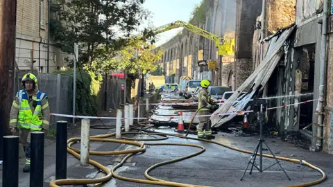 Smoke emerges from railway arches as firefighters spray water inside behind cordon