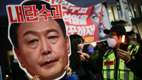 Getty Images A protester holding a cardboard reading "leader of insurgents" on an image depicting the face of South Korea's President Yoon Suk Yeol