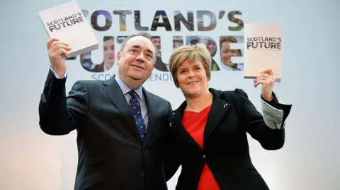 Getty Images Alex Salmond and Nicola Sturgeon holding copies of the White Paper for Scottish independence at a launch event in Glasgow in 2013. The publication, and the background, feature the words Scotland's Future.