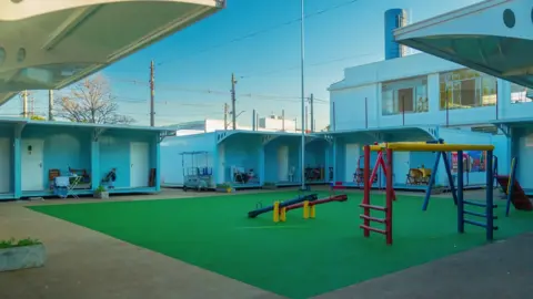 Blue container houses arranged in a square with a playground in the middle