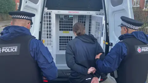 Photograph of a man being arrested and placed into the back of a police van during raids in the Derker area of Oldham