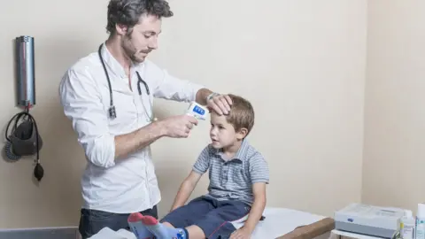 BSIP / Getty Images Doctor checking child's temperature