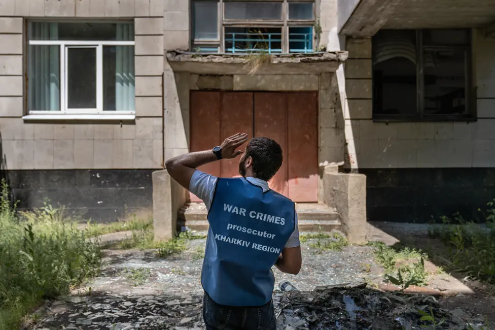 BBC A Kharkiv regional prosecutor inspects shell damage at an agricultural college near the city. Prosecutors have had to learn quickly how to conduct war crimes investigations.