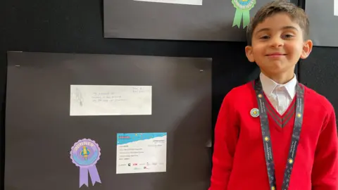 BBC Five year old boy in a red school jumper smiles with his winning engineering design