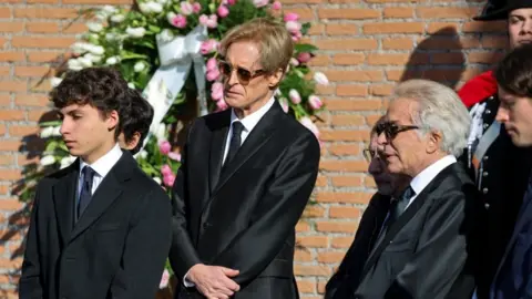 REUTERS/Yara Nardi Three men in black suits stand solemnly outside the church 