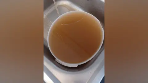 Brown water in white bowl on silver sink