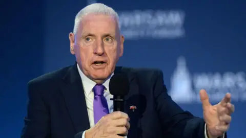 Getty Images Lord Coaker speaking at an event. He is holding a microphone and has short grey hair. He is wearing a black suit with a white shirt and a purple tie. 