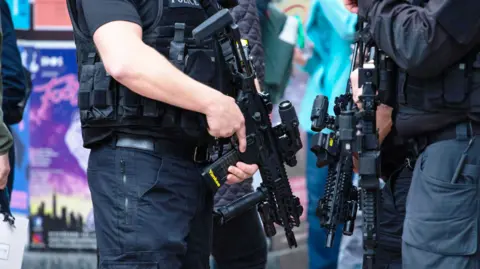Cropped image of the midriff of two counter-terrorism police officers wearing black uniforms, bullet-proof vests and holding assault rifles.