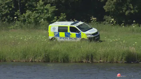 a police van is parked in long grass on the shoreside