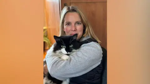 Nicci Knight A blonde woman holding a black and white cat.