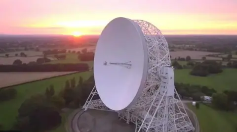 Jodrell Bank An aerial view of the large radio telescope in Jodrell Bank, Cheshire, with the sun setting over the countryside behind it.