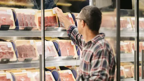 Getty Images Man in check shirt picks up a packet of raw beef from a supermarket fridge