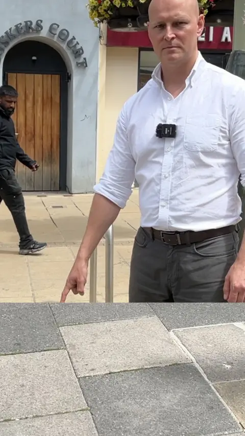Man pointing to the tarmac looking stern.
