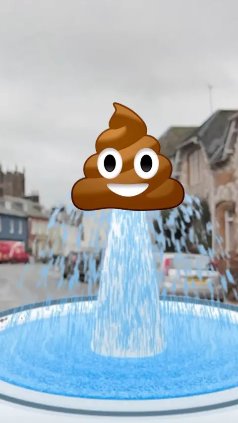 A smiling poo emoji on a fountain, sits on top of a fountain spurting blue water