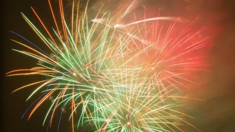 A fireworks display showing several exploding fireworks, in green and red, against a dark sky