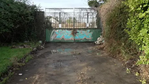The gates to a meanwhile site in Lockleaze, Bristol. There is a high security fence over the gate, which is covered in graffiti.
