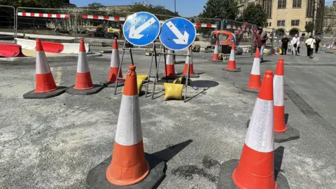 Orange and white traffic cones and metal barriers seal off an area of a city centre.