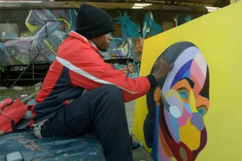 AFP A man is seen painting an abstract profile of a woman. The planes of her face are painted in different colours. He is using a brush to paint strokes of black on her hair.