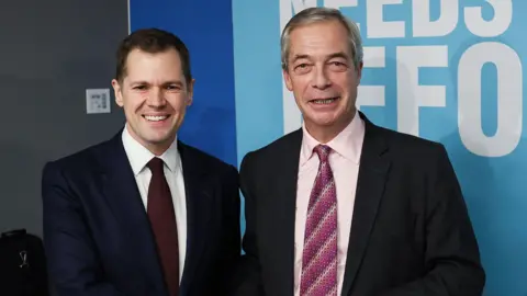 Former British Conservative Party member Robert Jenrick shakes hands with Reform UK leader Nigel Farage at a press conference, as Jenrick has announced he has defected from the country's Conservative Party to the right-wing Reform UK Party, in London, January 15, 2026.