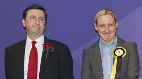 Getty Images The election count in 2015 - Douglas Alexander -  a dark haired man with a suit, red tie and red rosette, stands next to Mhairi Black, who has  blonde hair and is wearing a grey suit and an SNP rosette
