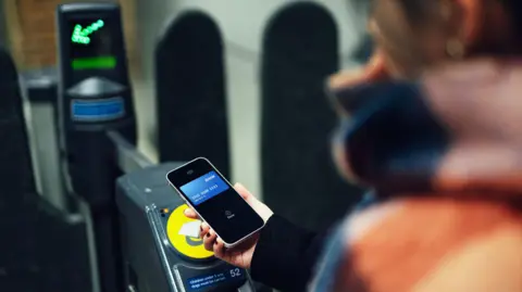 Young woman making contactless payment with smartphone at train station - stock photo