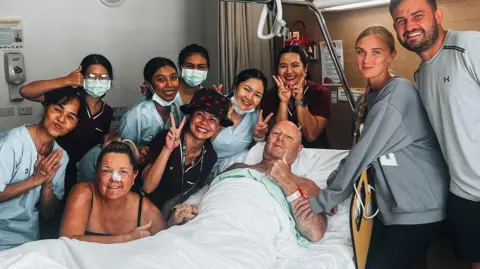 Lee Francis Lee Francis surrounded by family and nurses in hospital in Thailand