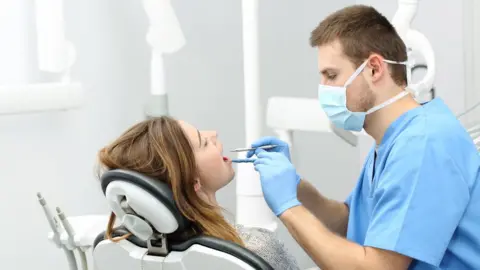 Getty Images Dentist treating a patient wearing a mask