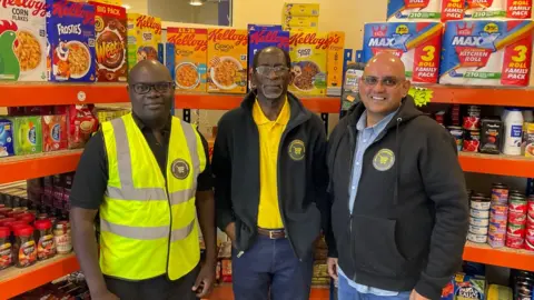 BBC Three men standing in front a stall at the supermarket