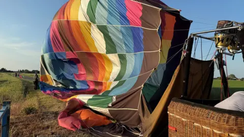 Cambridgeshire Police Brightly coloured deflated hot air balloon on side of rural road near fields.