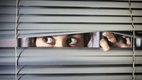 Getty Images Woman looking through a blind